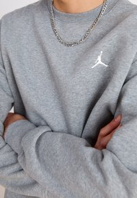 Szara bluza z okrągłym dekoltem, z białym logo Jumpman na piersi, zestawiona z warstwami srebrnych �łańcuszków. Miękka faktura, luźny krój.