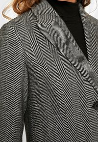 Chaqueta con patrón de pata de gallo en blanco y negro, con solapas de muesca y cierre de un solo botón. Confeccionada con tela texturizada.