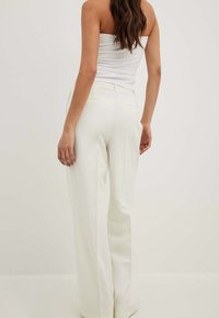White wide-leg trousers featuring a tailored fit with a smooth texture. Back view shows two back pockets and a clean waistband design.