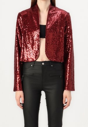 Red sequined cropped jacket with long sleeves, featuring a shawl collar. Paired with tight black pants, showcasing a sleek and shiny texture.