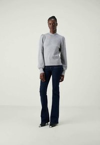 Maglione grigio a maglia con maniche a sbuffo, vita aderente, abbinato a jeans svasati blu scuro e scarpe con tacco a punta nere. Texture liscia, design classico.