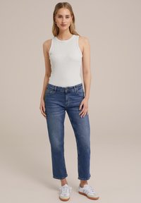 Vit ribbad linne, blå raka jeans och vita sneakers med gummisula. Enkelt mönster, avslappnad passform och minimala detaljer.