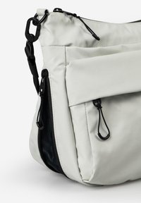 Borsa a tracolla bianca con tasche zip anteriori e laterali, cursori neri per le zip e una tracolla nera regolabile con chiusura in plastica.