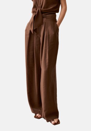 Bruine broek met hoge taille en wijde pijpen met voorplooien, gecombineerd met een bijpassende geknoopte mouwloze top en bruine sandalen met open teen.