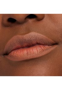 Nude läppstift applicerat på släta, fylliga läppar; matt finish med naturlig textur och mjuka konturer; rik brun hudton i närbild.