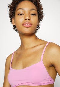 Top cropped rosa com alças finas, feito de um tecido suave. Apresenta um design simples, sem adornos, com um leve brilho.