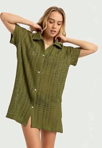 Grön, kortärmad virkatröja med krage, med knappstängning fram och sidslitsar. Texturen är öppen och har ett mönstrat design.