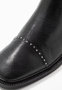 Botas de cuero negro con un acabado texturizado, diseño curvo y tachuelas plateadas decorativas a lo largo de la costura. Suela de goma resistente.