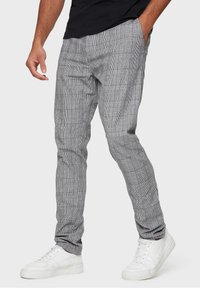 Pantaloni a quadri grigi in tessuto intrecciato, caratterizzati da una vestibilità aderente. Abbinati a sneakers bianche, con caviglia scoperta e mano in tasca.