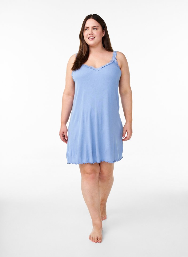 Žena kráča bosá, oblečená v svetlomodré sleeveless nočné šaty s čipkovou ozdobou na ramienkach a výstrihu na bielom pozadí.