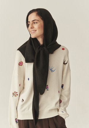 Pletený svetr v krémové barvě s barevnou květinovou a postavičkovou výšivkou; doplněn texturovaným černým šátkem uvázaným kolem krku.