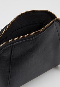 Svart läderpås med en texturerad utsida, en guldfärgad dragkedjestängning och ett fodrat inre med en extra dragkedjeficka.