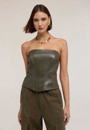 Haut en cuir sans bretelles de couleur vert olive avec une coupe ajustée, coutures accentuées, associé à un pantalon doux de couleur vert olive.
