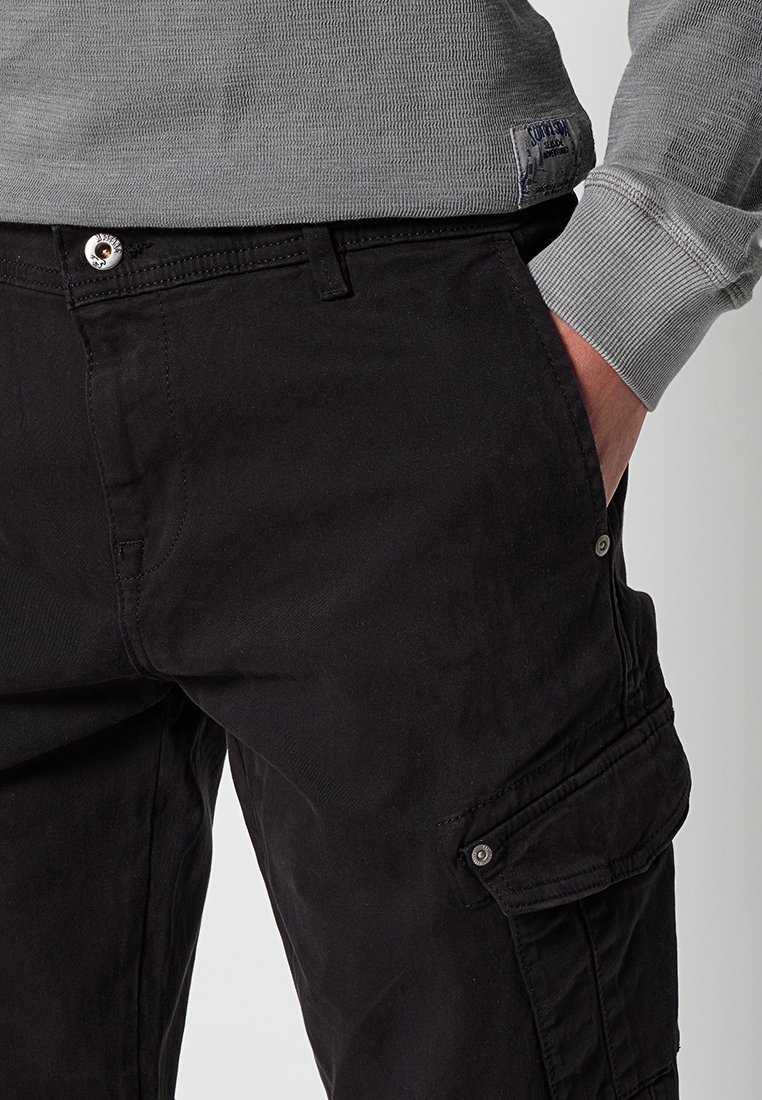 Zwarte cargobroek met een gladde textuur, voorzien van zijzakken, een knoopsluiting en een lichte glans. Gecombineerd met een grijze T-shirt met lange mouwen.