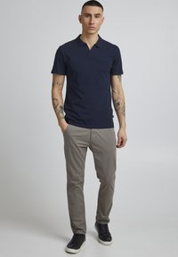 Marineblå polo skjorte med en diskret krage, kombinert med lysegrå bukser og svarte sneakers. Har kortermet design og en slank passform.