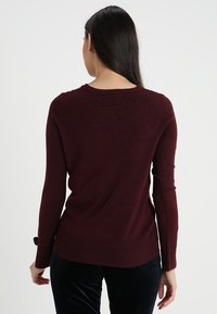 Burgundy sweater with long sleeves, ribbed hem and cuffs, soft texture, and a rounded neckline. Back view shows smooth fabric without details.