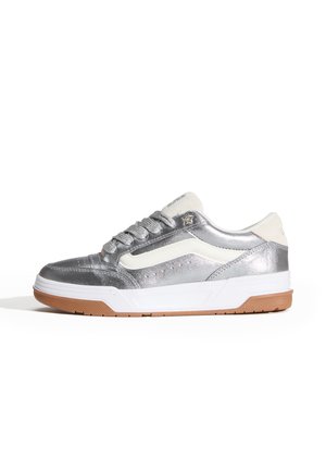 Zapatilla plateada metálica con detalles en blanco, parte superior texturizada, cuello acolchado y suela de goma color caramelo. Cuenta con cordones redondos y detalle de logo.