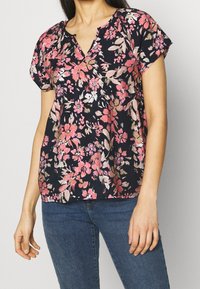 Námořnická květinová blůza s krátkými rukávy, zdobená růžovými a bílými květy. Výstřih do V se slabou řasenou detailou a lehký materiál.