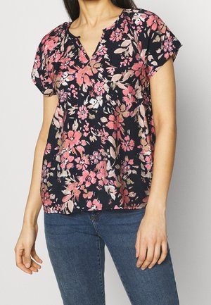 Blusa floreale blu con maniche corte, decorata con fiori rosa e bianchi. Scollatura a V con leggeri dettagli arricciati e tessuto leggero.