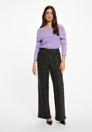 Maglione a coste lavanda senza spalle abbinato a pantaloni neri a vita alta con texture e gambe larghe, e scarpe nere a punta.