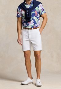 Camicetta a maniche corte floreale in navy, verde e rosa, abbinata a pantaloni corti bianchi e scarpe bianche. Maglione navy a tinta unita annodato attorno alle spalle.