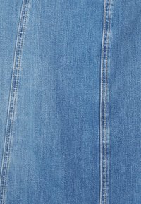 Modrý denimový materiál s hladkou texturou, viditelným stehem a mírně vybledlým vzhledem s vertikálními pruhy a švy.