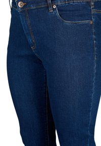 Tummansiniset farkut, joissa on slim fit -leikkaus, etutasku, metallipainike ja erottuva keltainen tikkaus saumoissa.
