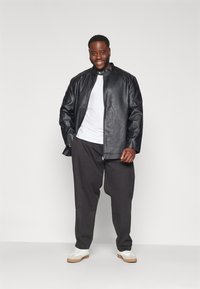 Chaqueta de cuero negra con un cuello alto, camiseta blanca debajo, pantalones grises holgados y zapatillas blancas; textura suave, diseño moderno.