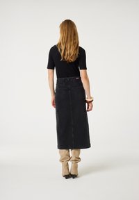 Zwarte denim maxi-rok met een aangesloten taille, achterzakken en een rechte snit, gecombineerd met beige aangesloten broek en puntige hakken.