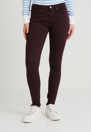 Vaqueros ajustados de color burdeos oscuro combinados con zapatillas blancas de plataforma y una camisa de manga larga a rayas azules y blancas.