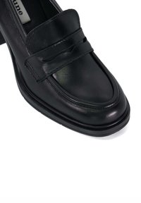 Black leather loafer with smooth texture, featuring a stitched band across the front and a low, solid heel. Simple design and classic shape.