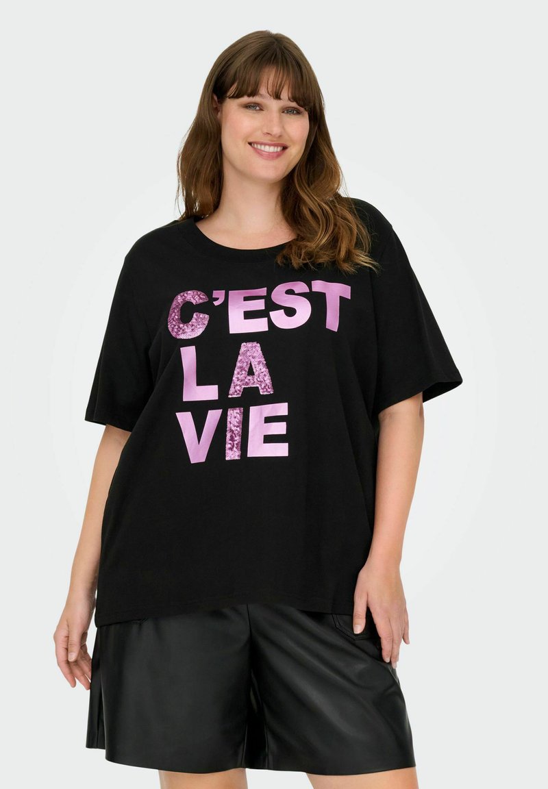 Camiseta negra de gran tamaño con el texto en lentejuelas rosas "C’EST LA VIE". Tela suave, cuello redondo y mangas cortas combinadas con pantalones cortos de cuero.