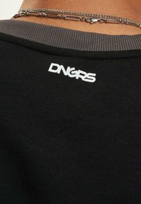 Black sweatshirt with ribbed neckline featuring white "DNGRS" logo at the back. Smooth texture, short-chain silver necklace visible.
