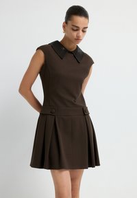 Braunes ärmelloses Kleid mit strukturierter Passform, plissiertem Rock und einem schwarzen, mit Pailletten besetzten Kragen. Verfügt über zwei dekorative Knöpfe an der Taille.