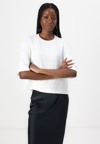 Tricou alb scurt, cu un model texturat, mâneci scurte și decolteu rotund; asortat cu o fustă din satin bleumarin. Finisaj albastru neted.