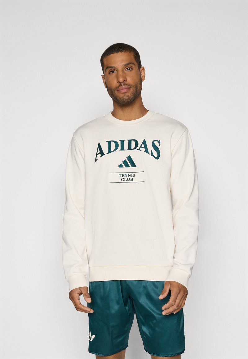 Sweatshirt crème avec "ADIDAS TENNIS CLUB" imprimé en vert foncé. Assorti avec un short teal arborant un logo blanc. Texture de tissu lisse.