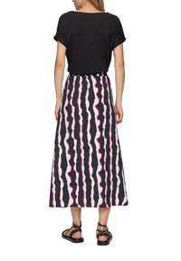Zwarte korte mouwen top gecombineerd met een lange rok met golvende zwart, wit en roze strepen. Model draagt zwarte sandalen met bandjes.