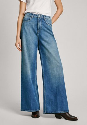 Wide-leg denim jeans in medium blue wash with a smooth texture. Features a high waist, front pockets, and straight hems. Paired with black boots.
