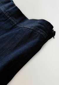 Tamsiai mėlyna džinsinio audinio medžiaga, turinti lygų paviršių, su užtrauktuku viršuje ir švariais siūlės kraštuose.