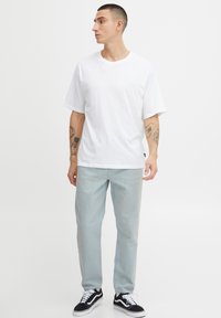 Camiseta de algodón blanca de manga corta, combinada con jeans de mezclilla azul claro y zapatillas negras. Presenta un corte relajado y un diseño sencillo.