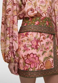 Floral-patterned dress with pink base, green trim, and intricate waistband. Features long sleeves and puffed cuffs with detailed embroidery.
