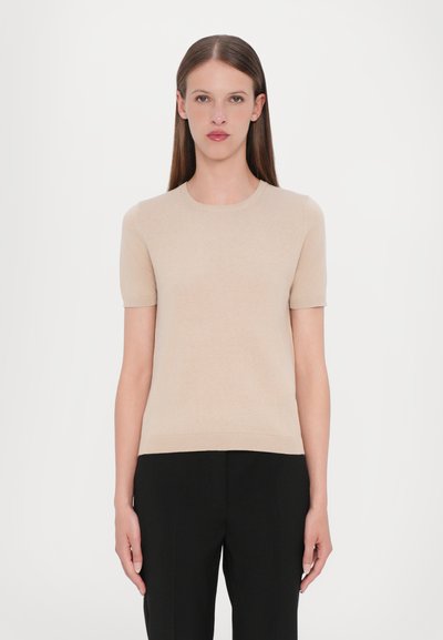 Top de punto de manga corta beige con escote redondo y dobladillo recto, combinado con pantalones negros de corte sastre. Textura suave y diseño ajustado.