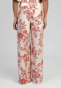 Des pantalons larges à motifs floraux présentent un fond crème avec des motifs de fleurs rouges et roses, une taille élastique et un tissu doux et léger.