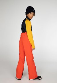 Felgroene skibroek, marineblauwe en gele lange mouwen top, zwarte beanie en zwarte schoenen met witte accenten. Rechte pasvorm.