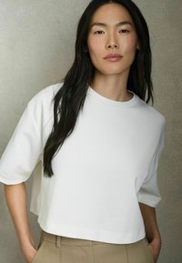Hvid cropped t-shirt med korte ærmer, lavet af blødt stof. Glat tekstur, rund halsudskæring, båret med beige høj talje bukser.
