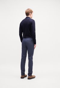 Temno modri slim-fit hlače z zadnjimi žepi in rjavimi čevlji. Nosijo se z dolgim črnim majico z dolgimi rokavi, ki ima gladko, mat teksturo.
