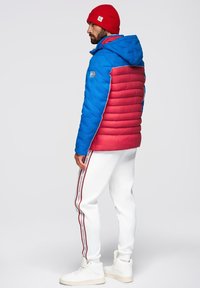 Blå och röd puffjacka med huva, kontrasterande paneler och sidostråk. Matchad med vita sweatpants med röda randaccenter.