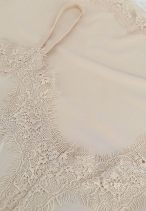 Nude top bez rękawów z misternym koronkowym wykończeniem wzdłuż dekoltu i hemu, charakteryzujący się miękką, gładką teksturą oraz delikatnym, postrzępionym brzegiem.