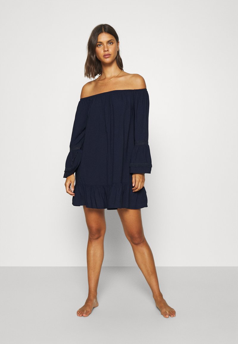 Vestido azul marino sin hombros con mangas largas en campana, dobladillo acampanado y detalles de encaje, confeccionado en una tela ligera.