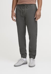 Dark gray jogger pants with elastic cuffs and waistband, featuring a drawstring. Worn with light gray athletic shoes.